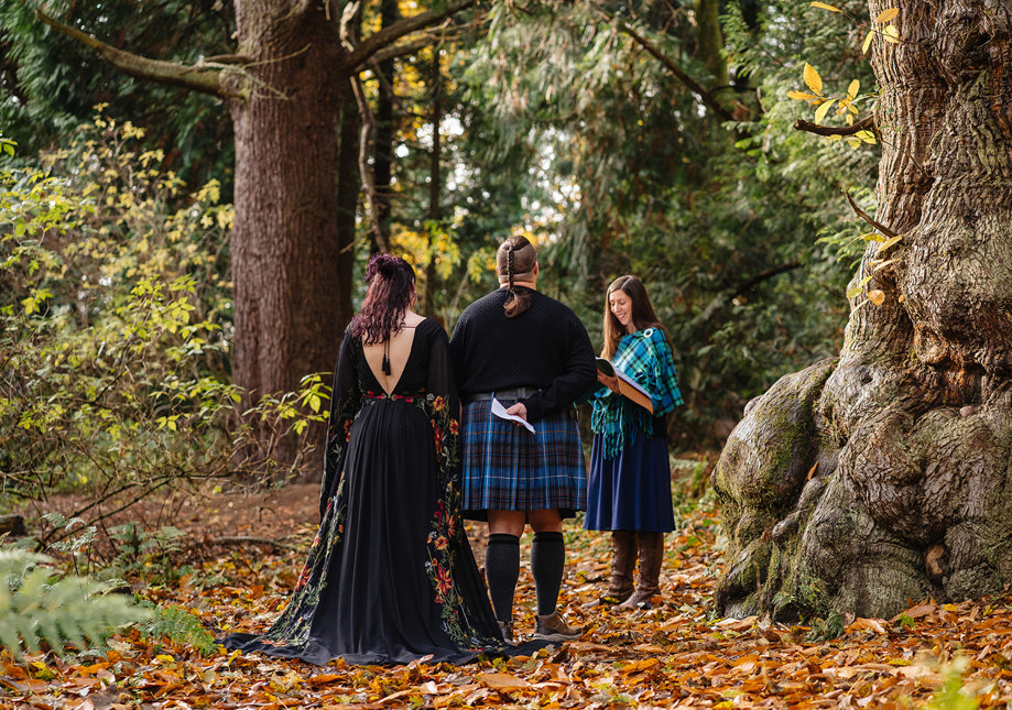 Celebrant Emily Porth at a woodland handfasting ceremony in autumn with the happy couple, standing next to an incredible ancient tree. Photo by Rachel Hein. 